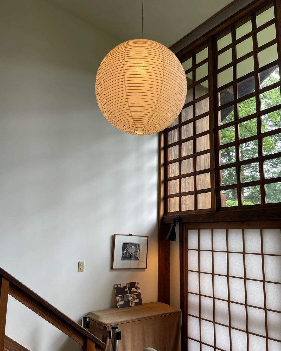 Glowing paper globe on a black cord above a wood stair rail beside a lattice window and framed photograph