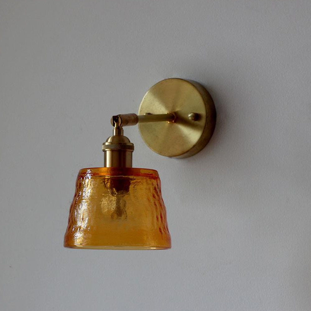 Close view of unlit amber-orange textured shade with gold-tone arm and round plate against gray wall
