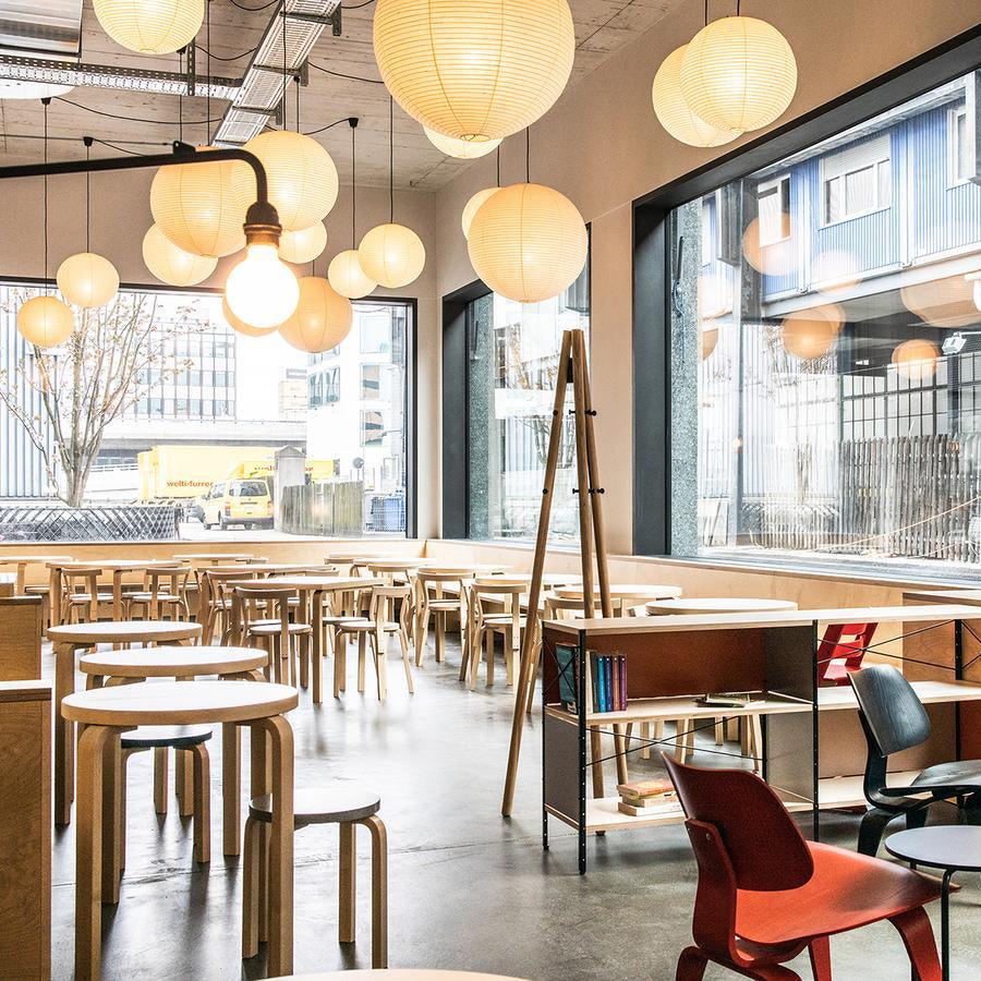 Several glowing paper globes in a cafe above round and long wood tables with books and a red chair
