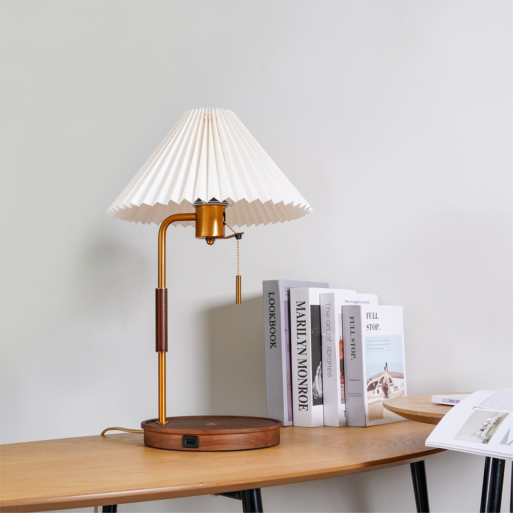 Walnut lamp with a white pleated shade and front USB port on its brown base beside books and an open magazine