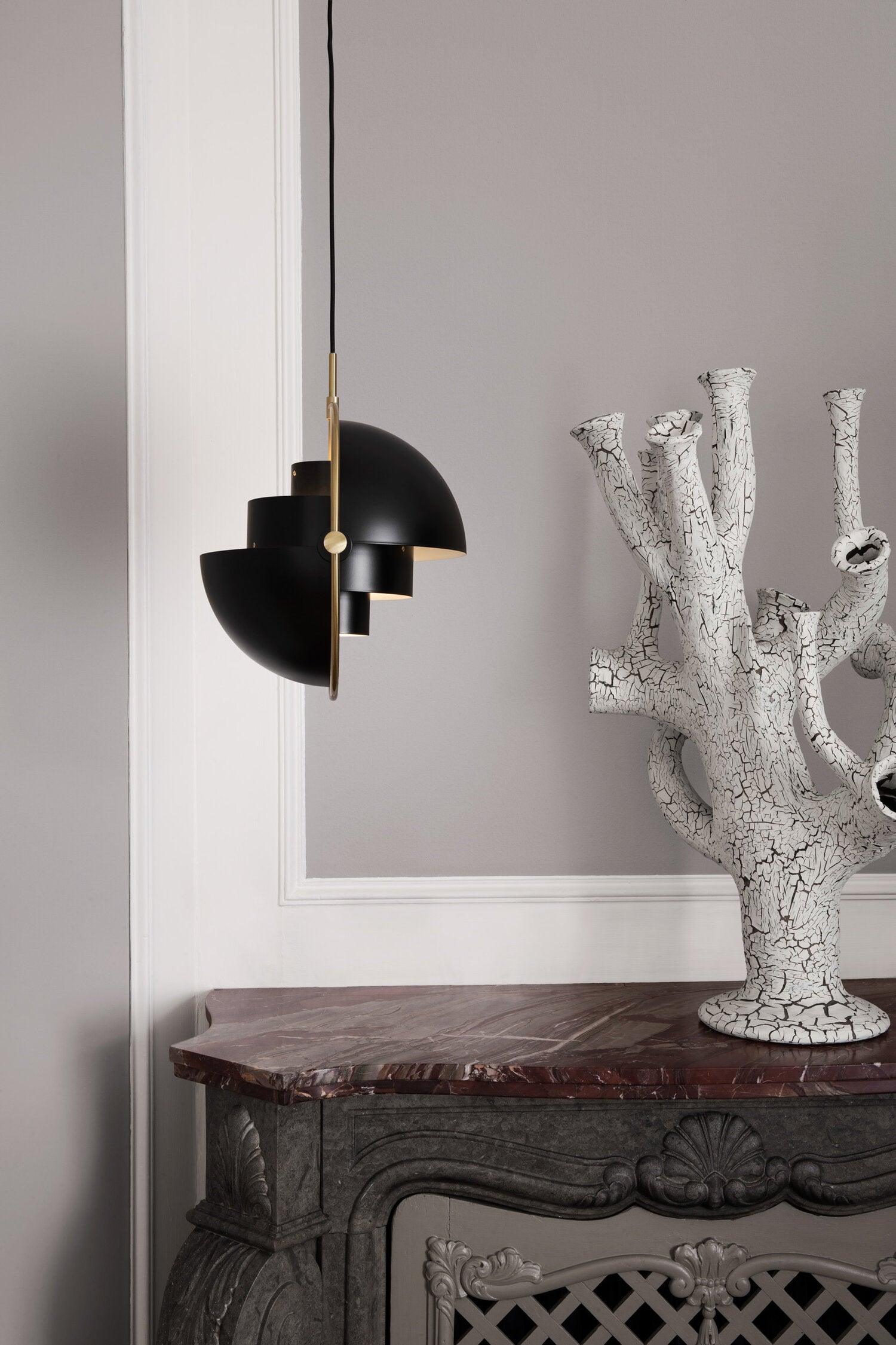 Black shade halves rotated apart beside a sculptural branch ornament.