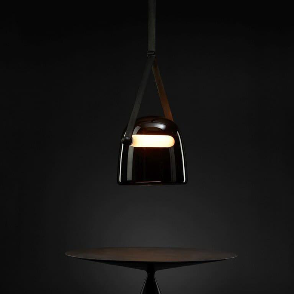 Dark glass pendant with split strap and glowing horizontal bar above a round table in a dim room