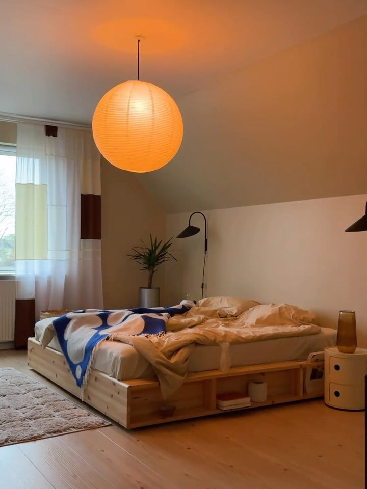 Warm-looking paper globe above a wood bed with blue blanket beside wall lamps and colour-block curtains