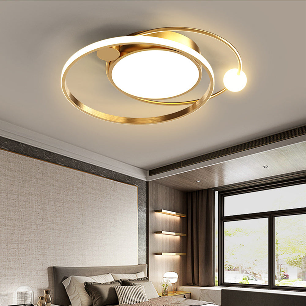 Gold-tone orbital ceiling fixture with bright disk and small sphere above a gray bedroom near shelves and windows