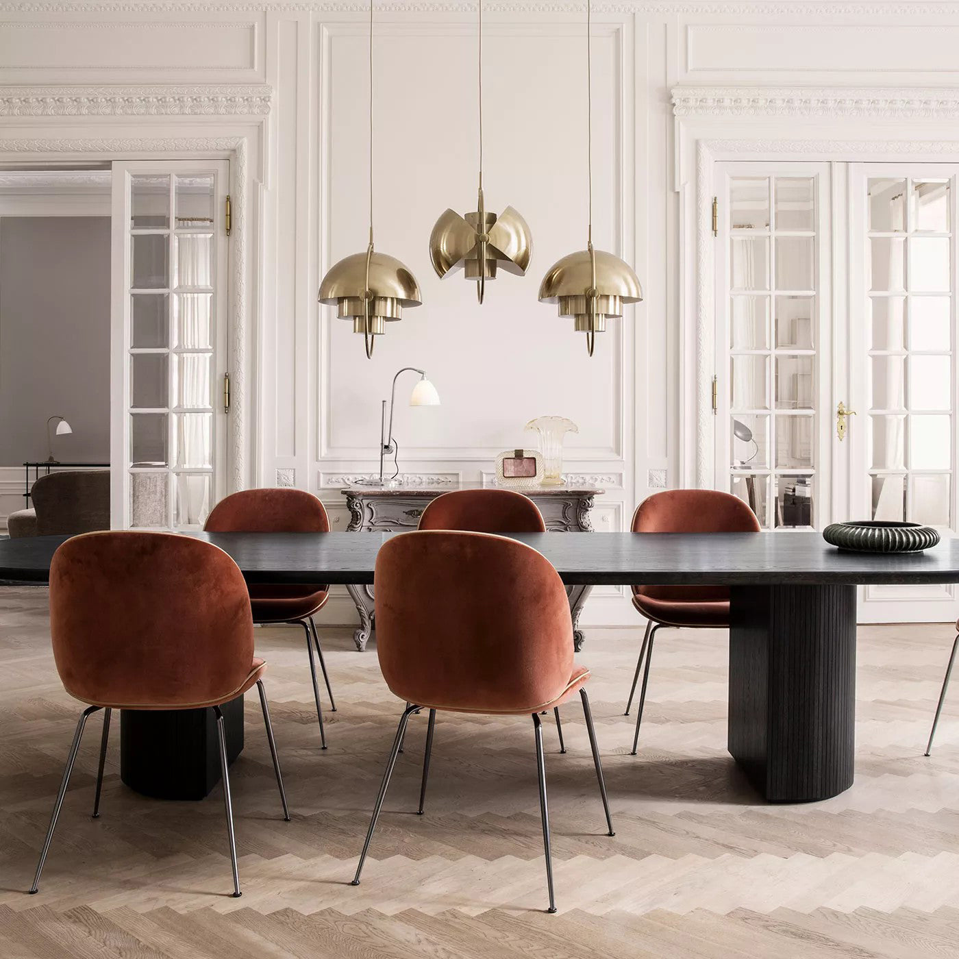 Three gold-toned pendants with different shade positions over a long dining table.