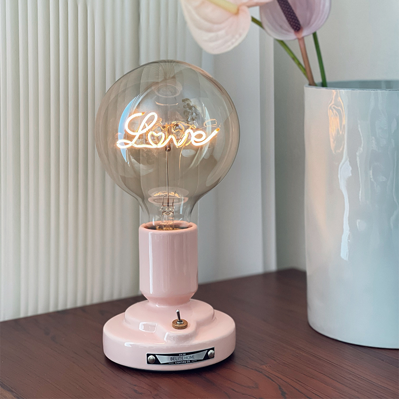 Pink-base Love-lettering globe lamp beside a tall pale blue vase with pink blooms on a dark wood table