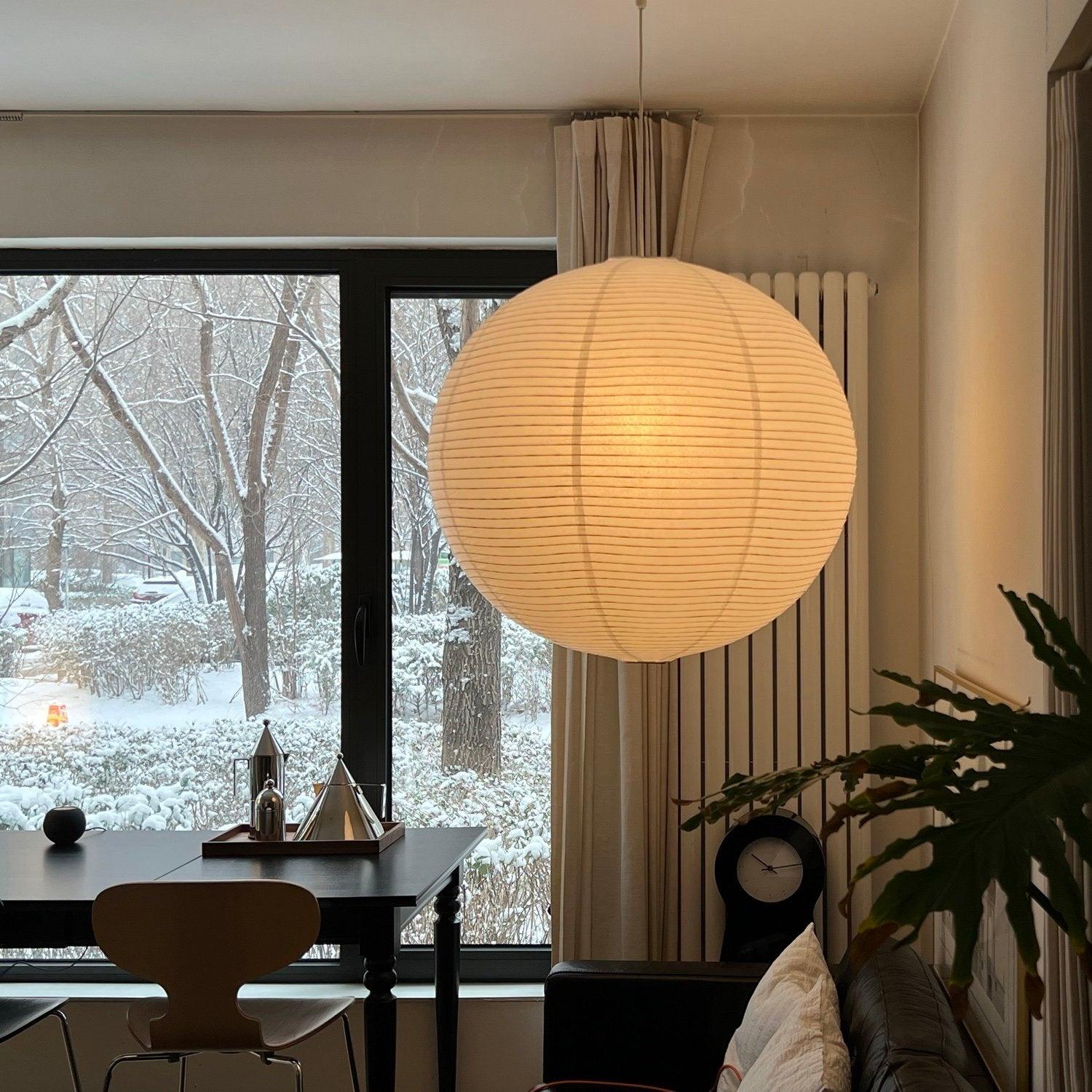Paper globe by a snowy-view window above a black table, wood chair and brown leather seat
