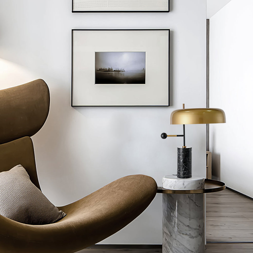 Table lamp with black veined base on a separate white veined side table near a tan chair and framed photos