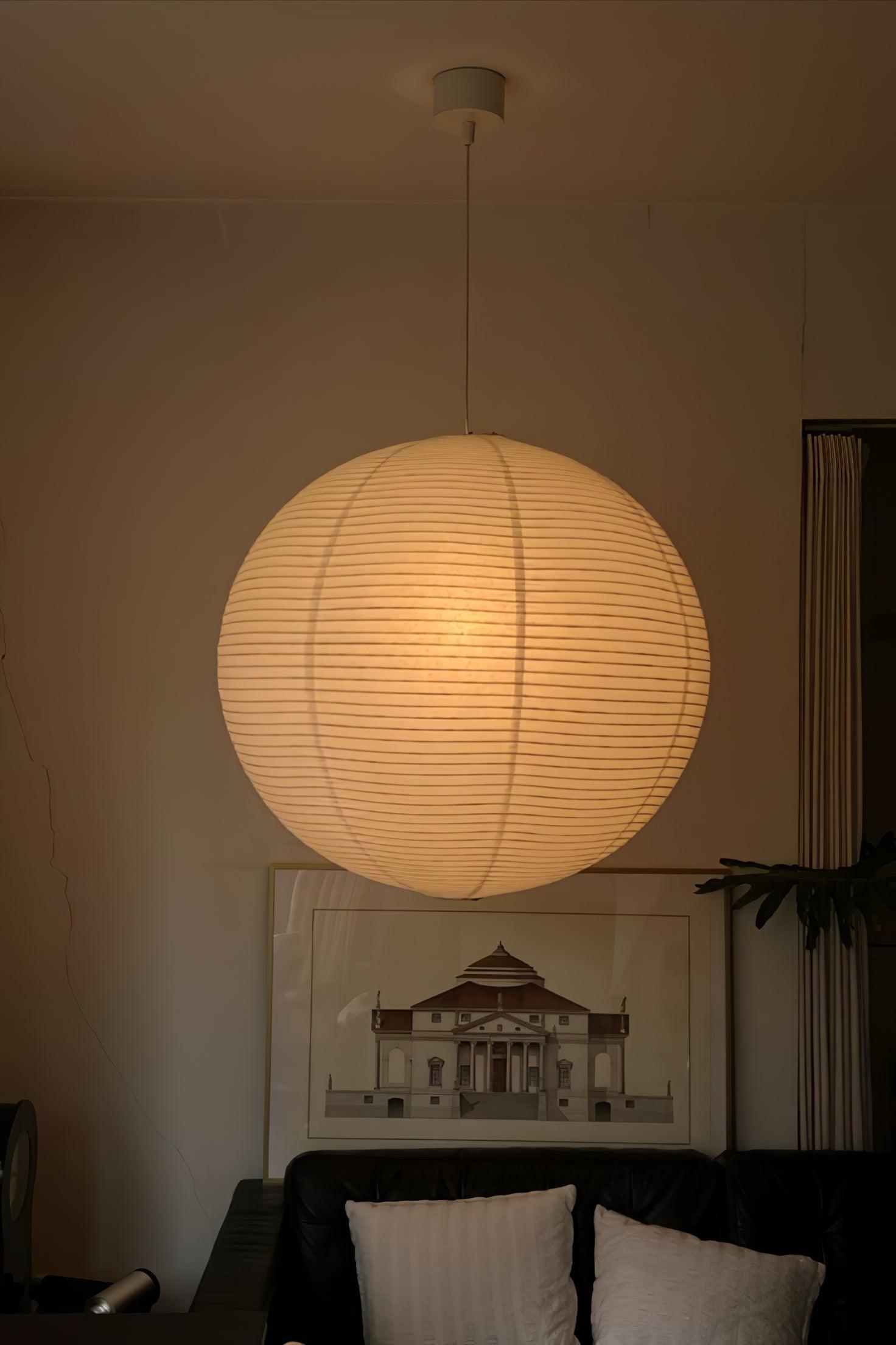 Glowing globe on a short white cord above a black sofa and framed architectural artwork