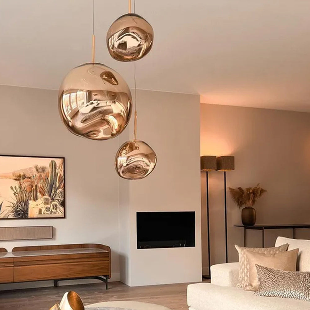 Three reflective Gold irregular shades above a wood sideboard beside cactus artwork, a fireplace and cream seating