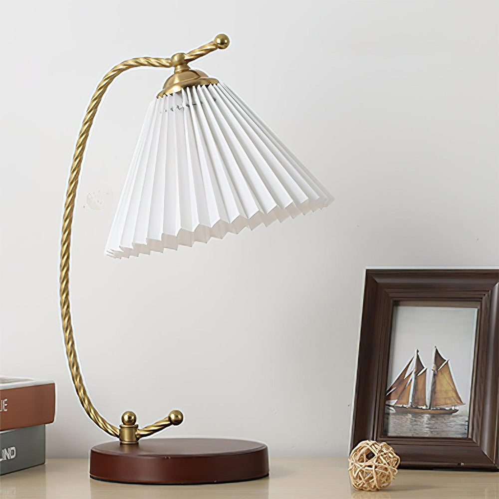 White Dotty lamp with tilted pleated shade beside books, framed sailboat art and a woven ball
