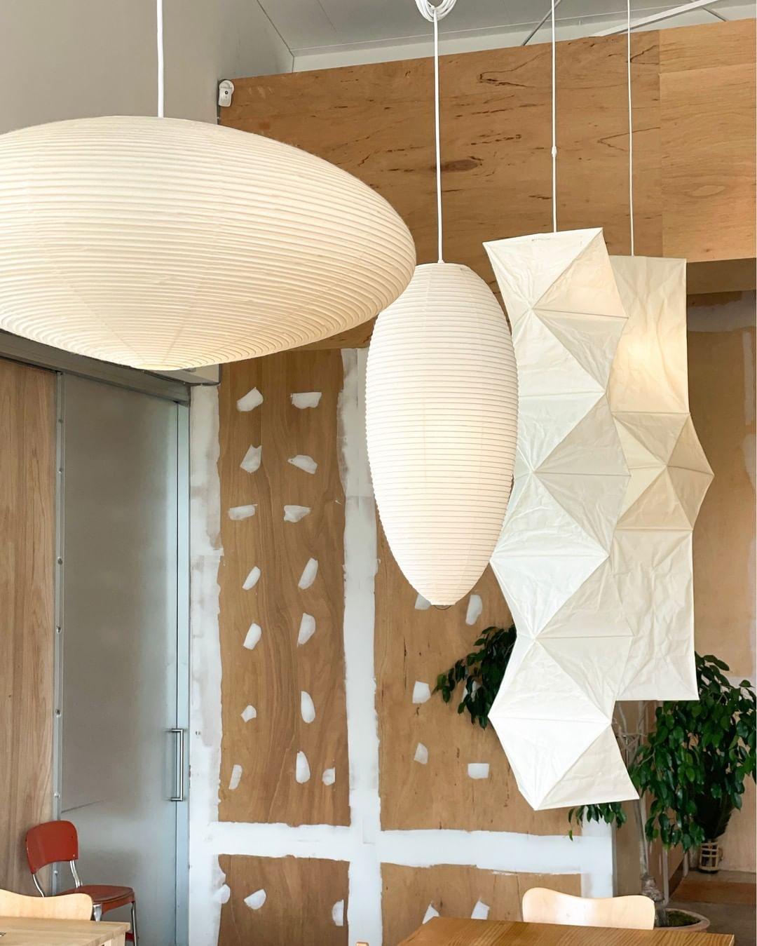 Flattened, oval and faceted paper shades displayed before a plywood wall with a red chair and plant