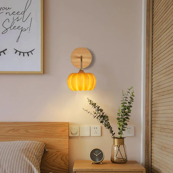 Yellow pumpkin wall light above a bedside table with a clock and foliage beside a wooden headboard