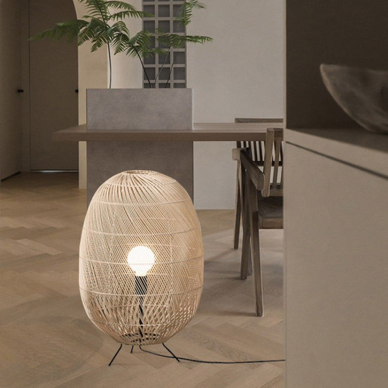 Oval woven lamp on wood floor beside dining table, slatted wooden chair and fern planter