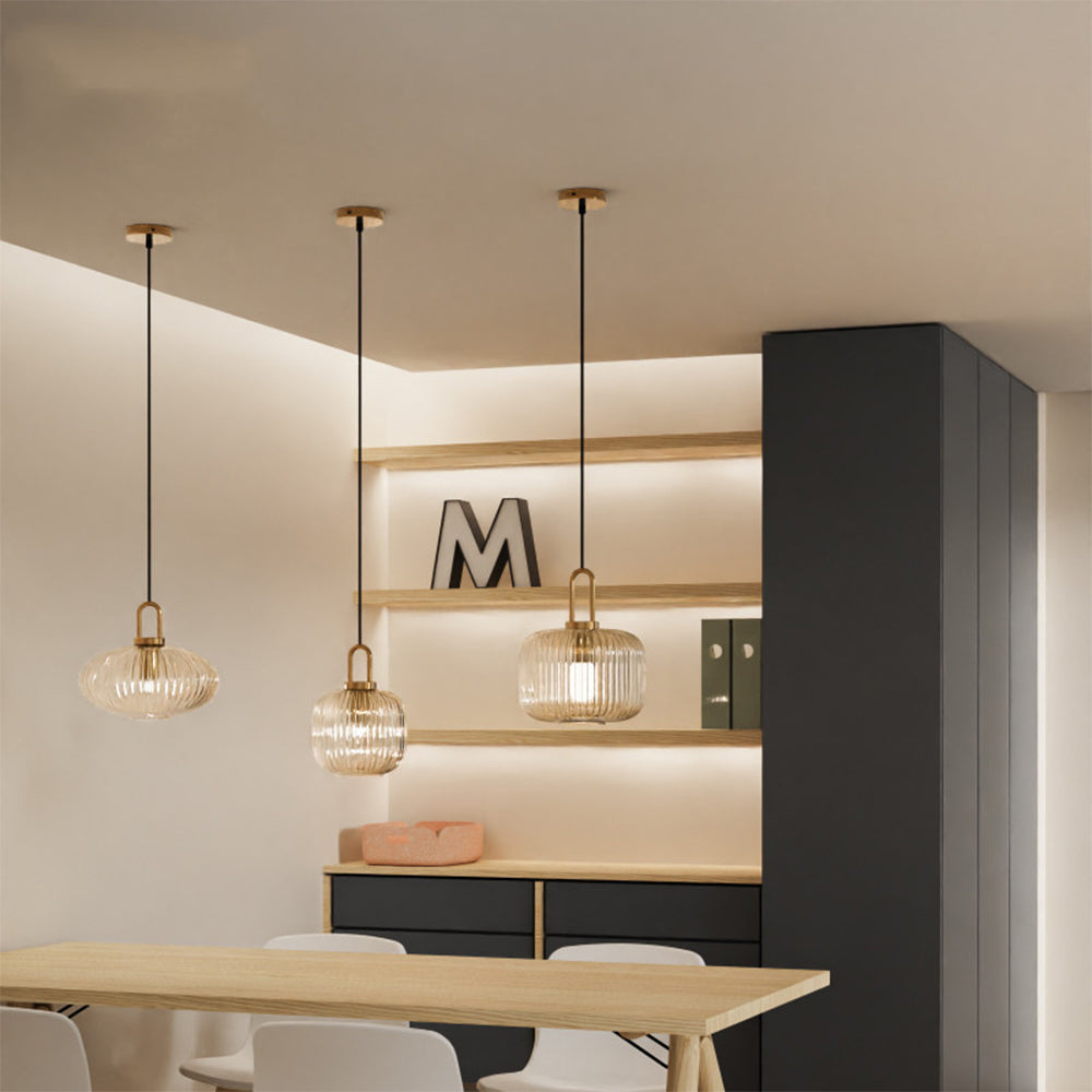 Three clear ribbed glass pendants in different profiles above a dining table
