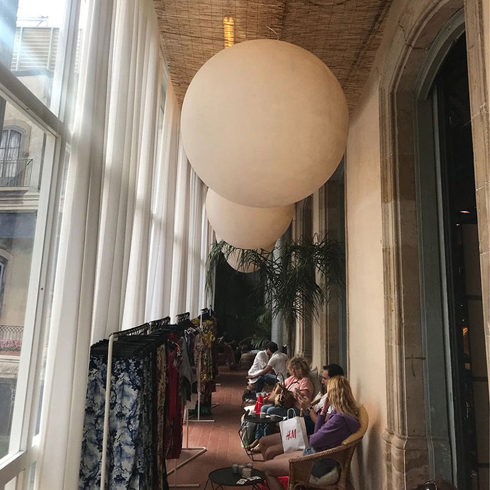Large pale globe pendant and smaller spheres in a window-lined lounge with curtains and seating