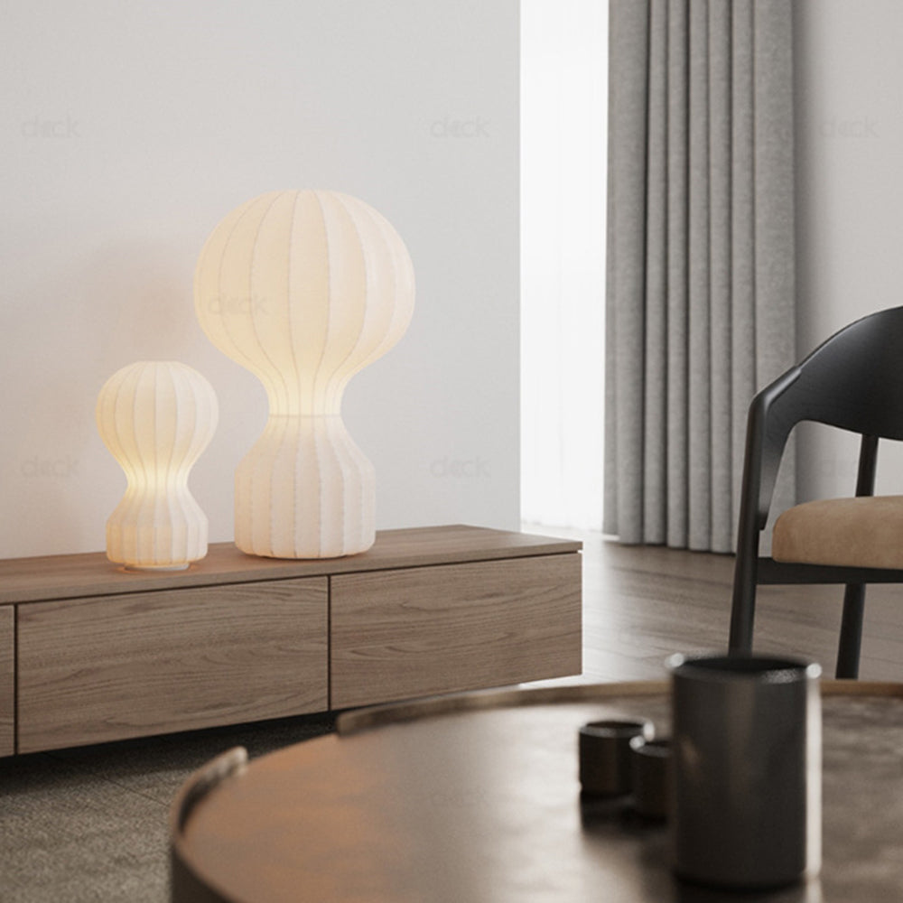 Small and tall cream-looking ribbed lamps glowing on a wooden low cabinet near grey curtains and a dark chair