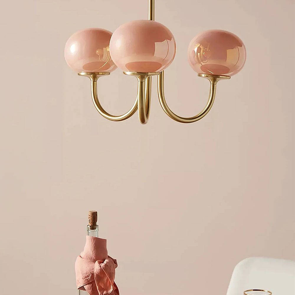 Pink glass globes and gold-tone curved arms above a dining setting with a bottle and chair