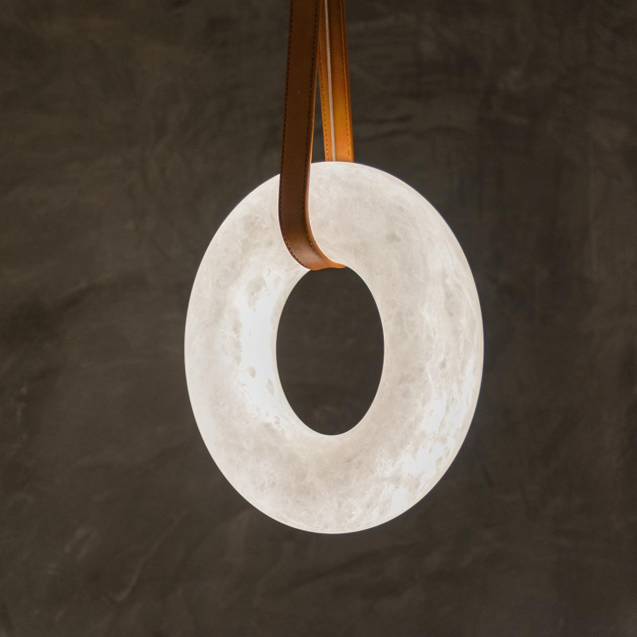 Vertical white ring suspended on a lighter brown strap against a textured wall.