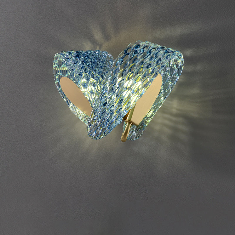 Lit two-loop blue glass wall light with oval texture and gold-tone inner plates on a gray wall