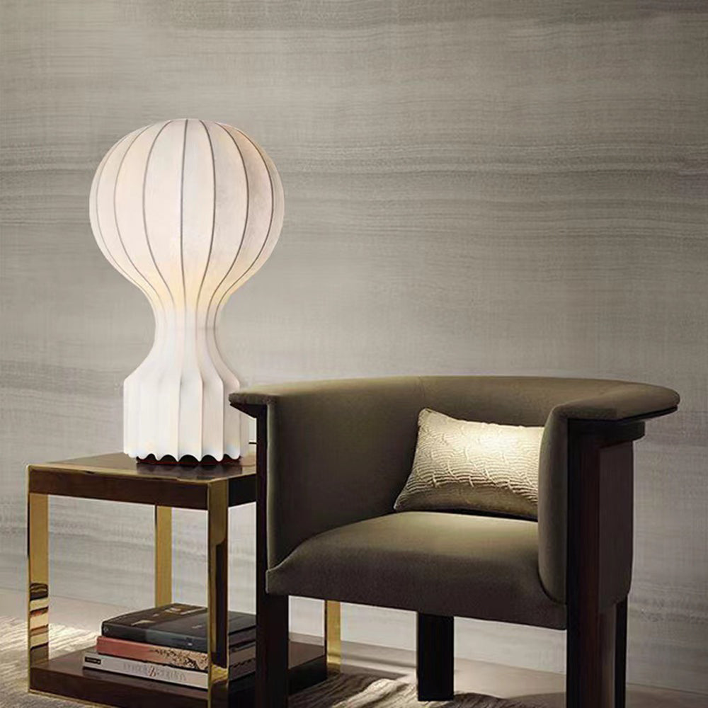 Pale ribbed lamp on a gold-tone side table left of a dark wooden armchair, with books on the lower shelf