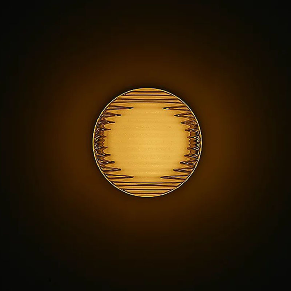 Front of a warm-lit round fixture with horizontal ribs on a black background