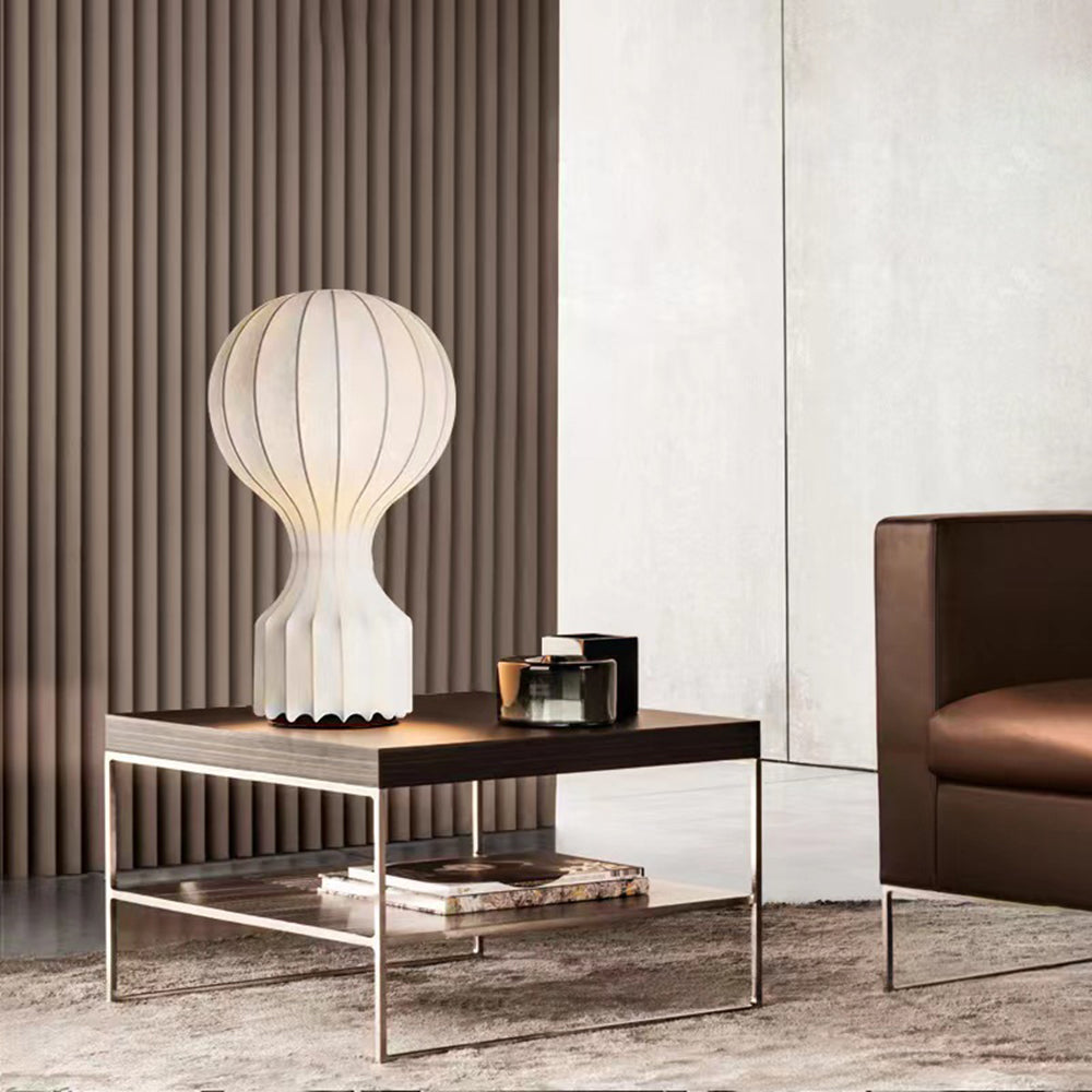 Wide view of the ribbed lamp on a dark wooden low table with a silver-tone frame, brown chair and vertically slatted wall
