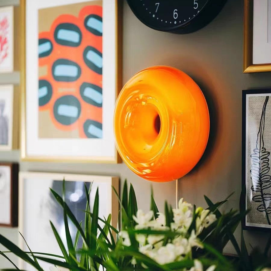 Orange donut wall light among framed prints and a black clock with white flowers in front