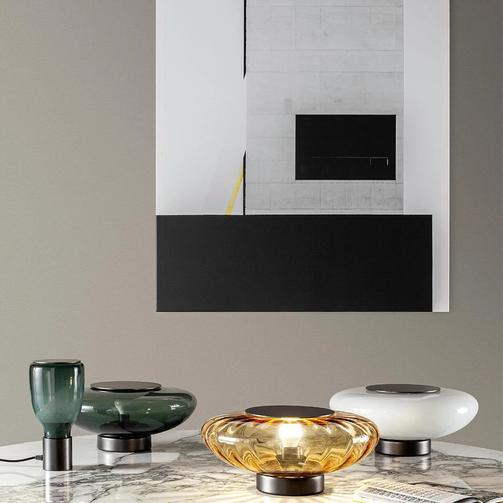 Tall green bottle-shaped lamp at left beside wider green, amber and white bowl-shaped lamps under abstract artwork