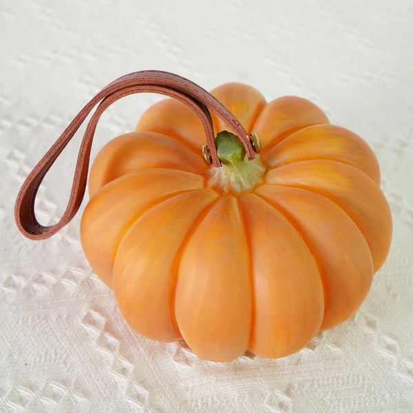 Overhead detail of unlit pumpkin lamp, brown loop strap, gold-toned fasteners and green stem on lace cloth