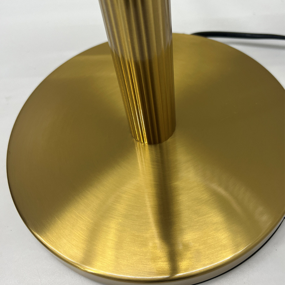 Close view of the brushed circular gold-tone foot and lower fluted column, with a black edge underneath and cord behind