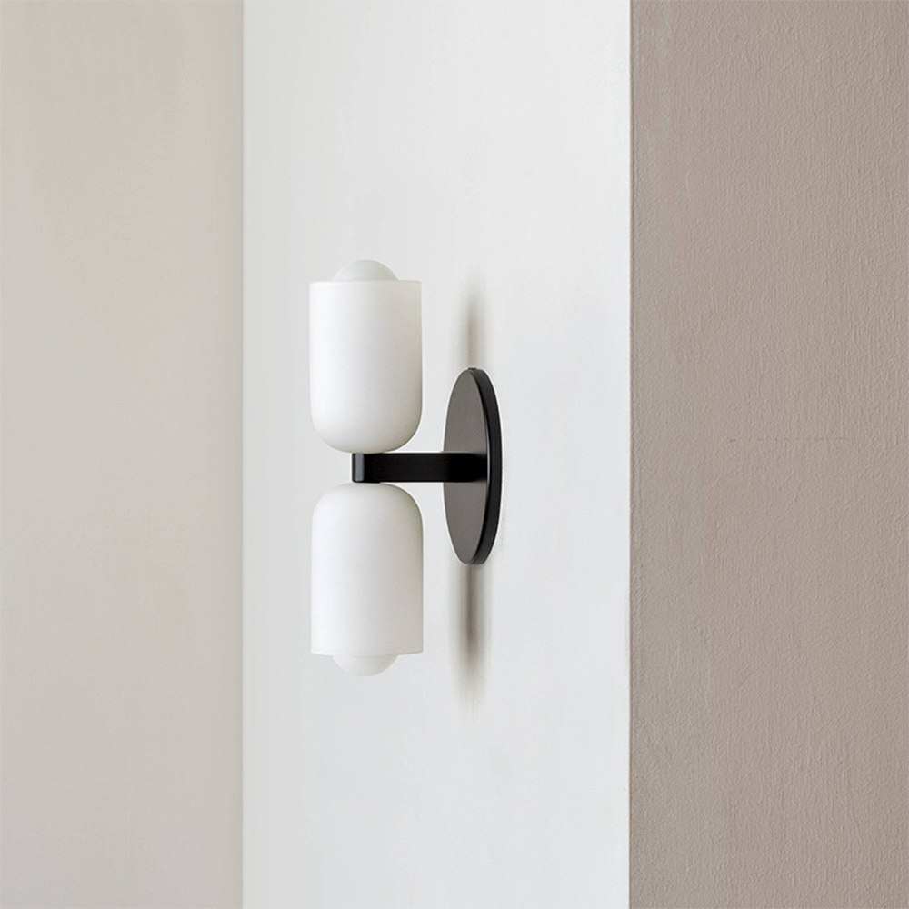 Side view of black double-head sconce beside a wall corner, showing its support arm and white shades