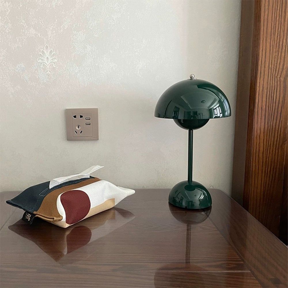 Green table lamp on polished wood beside a patterned tissue cover and wall outlet
