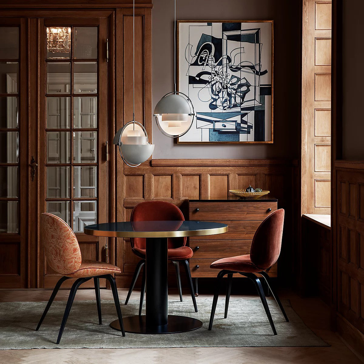 Two ring pendants hanging near artwork in a wood-panelled dining space.
