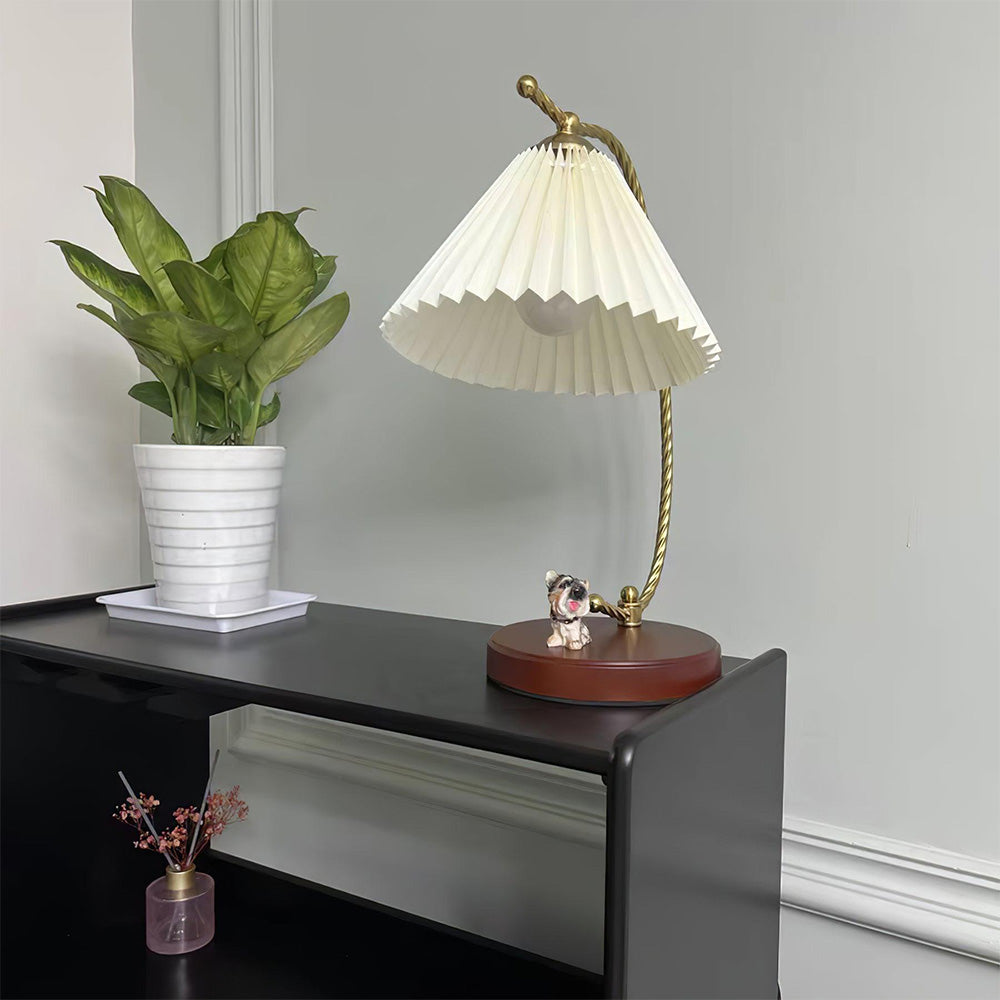 White pleated lamp viewed from below on a black console beside a plant and dog figurine