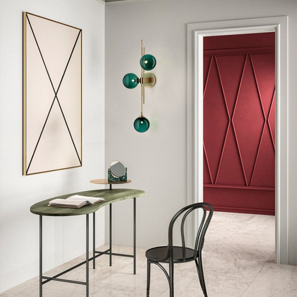 Green globe wall light above a narrow green console with an open book and small mirror beside geometric artwork and a red patterned door