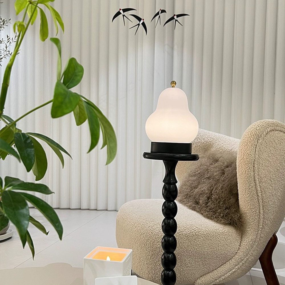 Pear-shaped lamp on a black sculptural side table beside a beige textured armchair, leafy plant and bird mobile