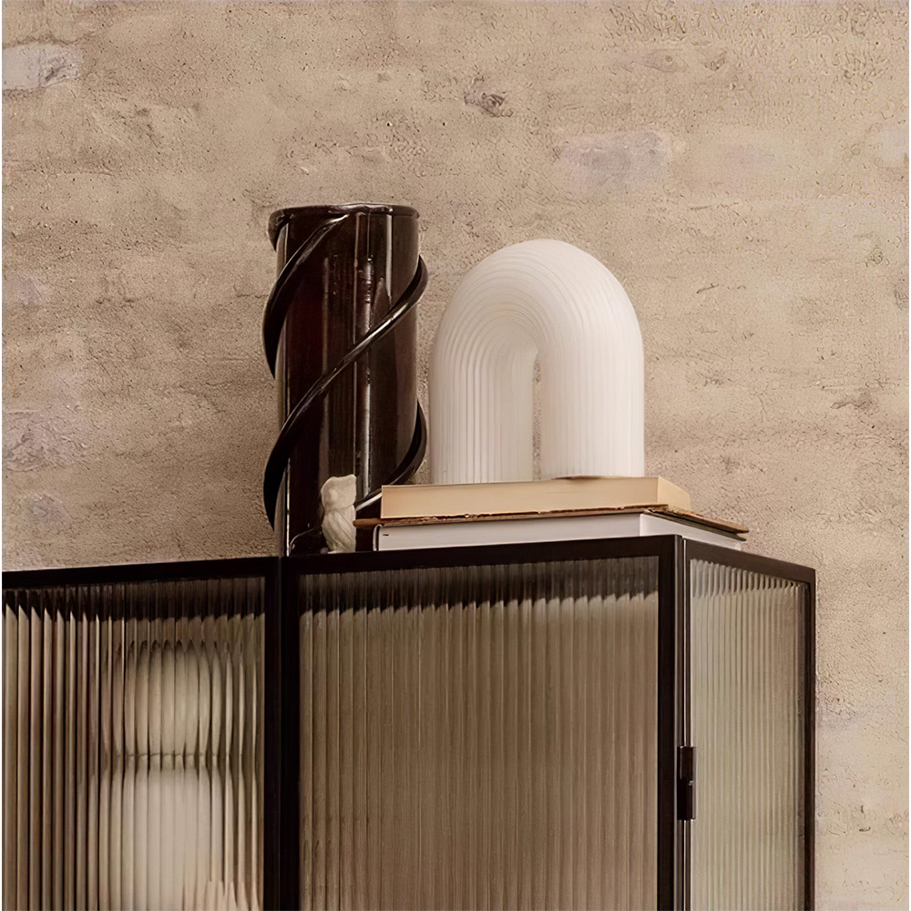 Arch lamp partly behind books on a ribbed-glass cabinet beside a tall dark vase