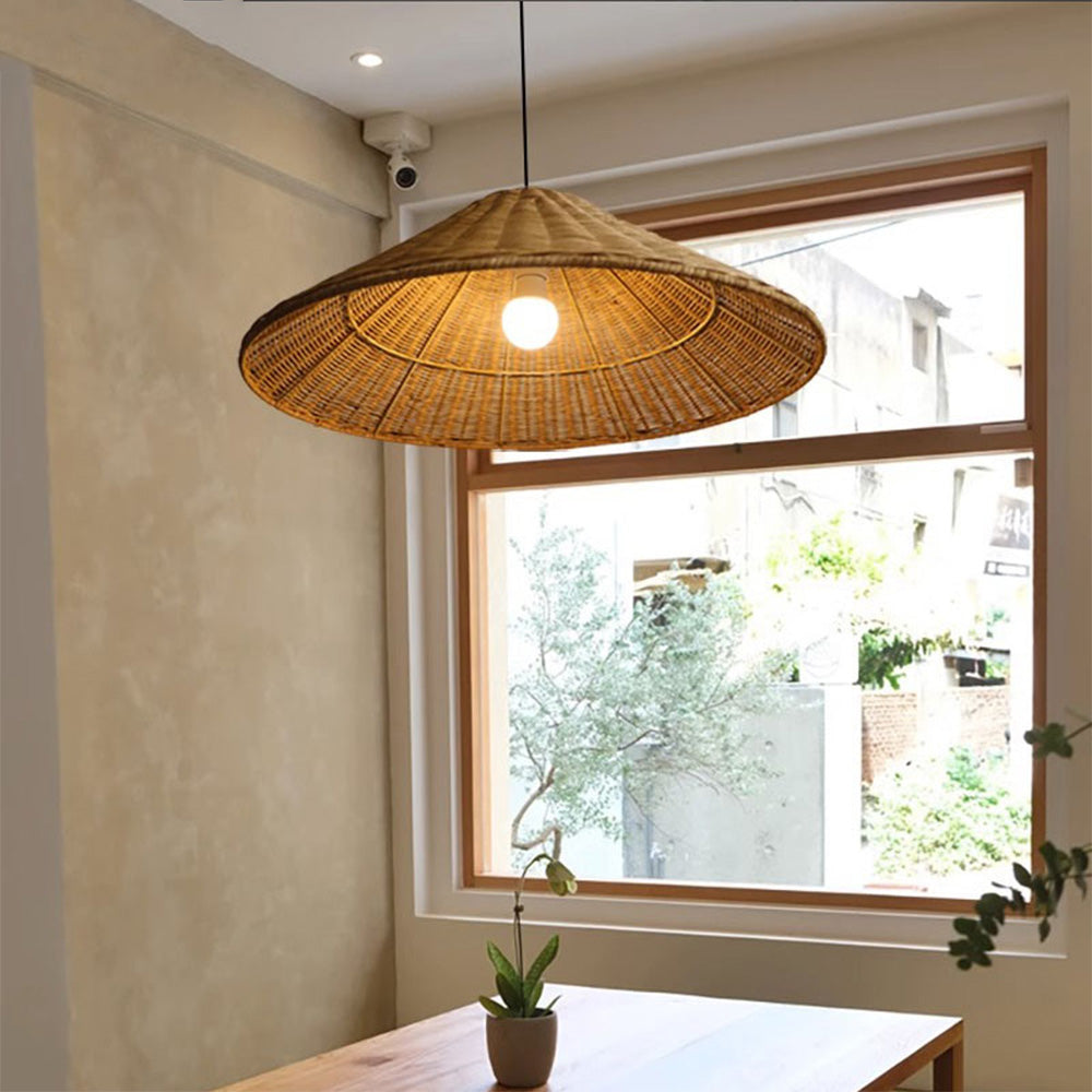 Lit Brown rattan cone pendant above a wooden table and potted plant beside a large framed window