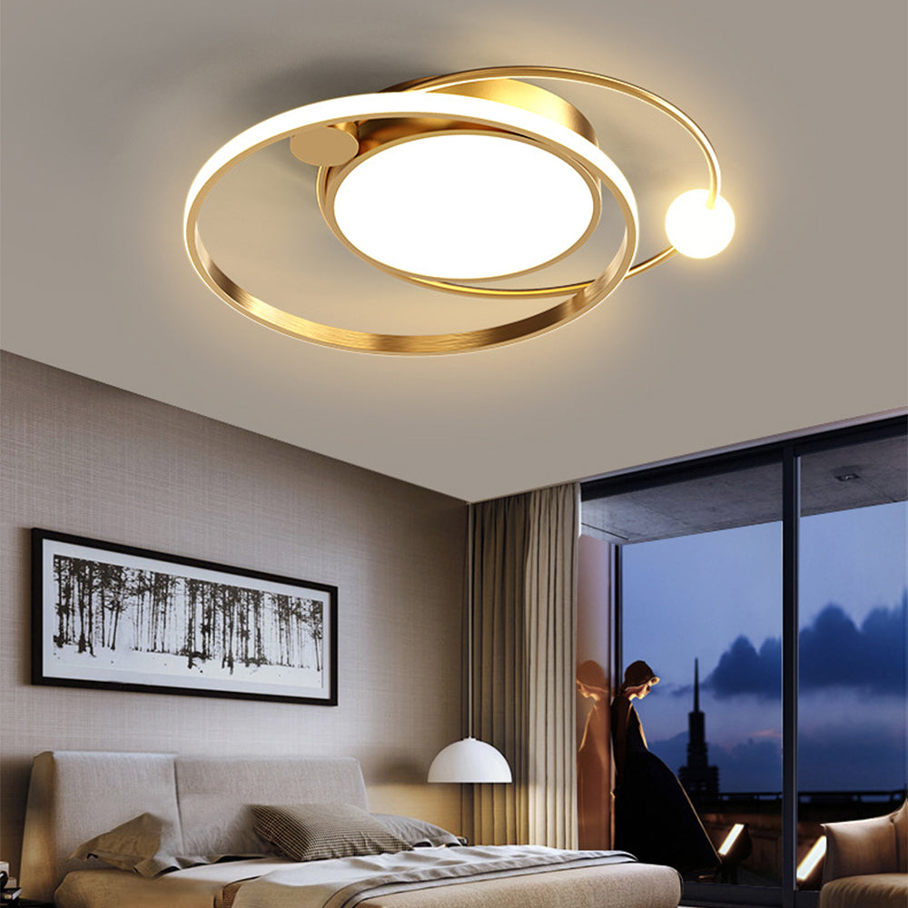 Gold-tone orbital ceiling fixture above a bedroom with framed forest art and a window at dusk