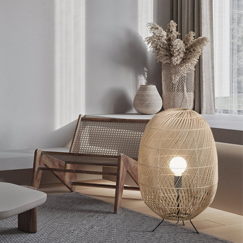 Oval rattan lamp beside a timber cane chair and pale coffee table, with patterned vase and dried grasses near window