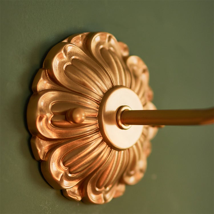 Close-up of embossed gold-toned floral wall plate with central arm and visible fastener heads