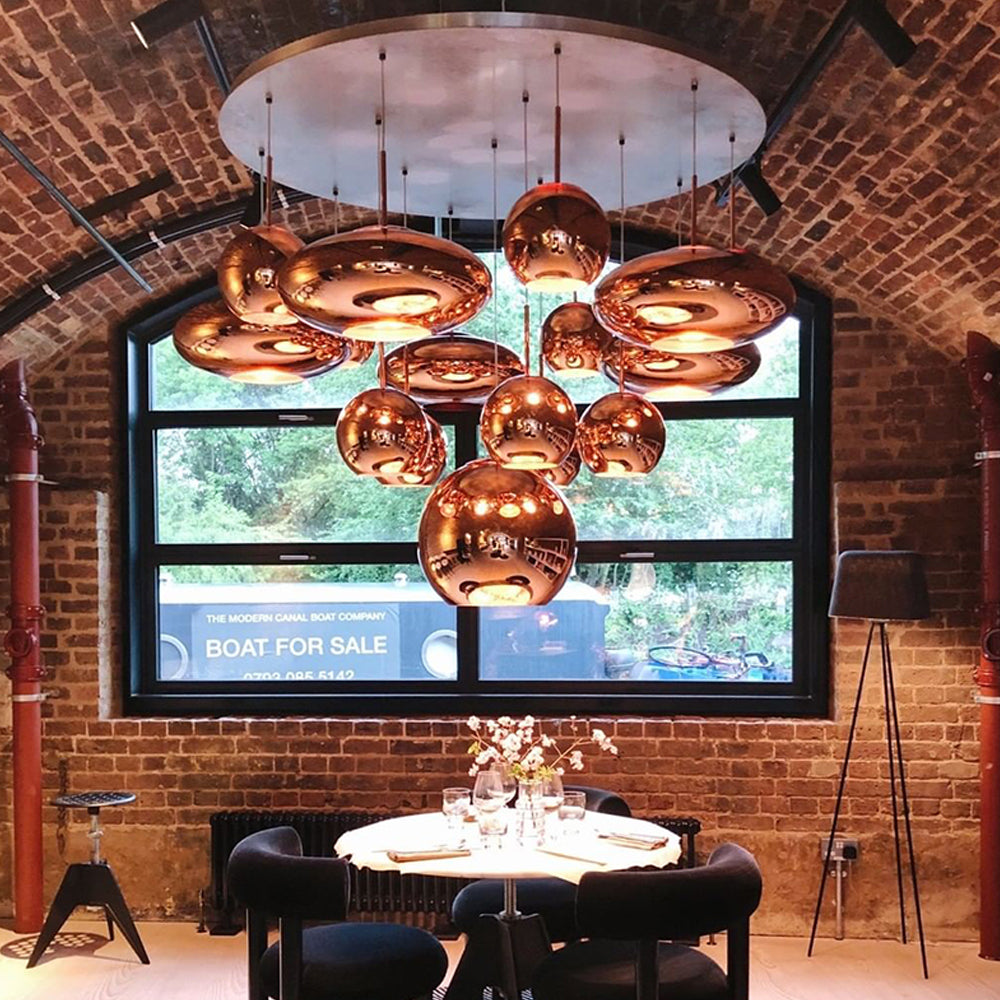 Smooth copper-coloured globe and flattened disc shades over a white round table in a brick-vaulted dining room