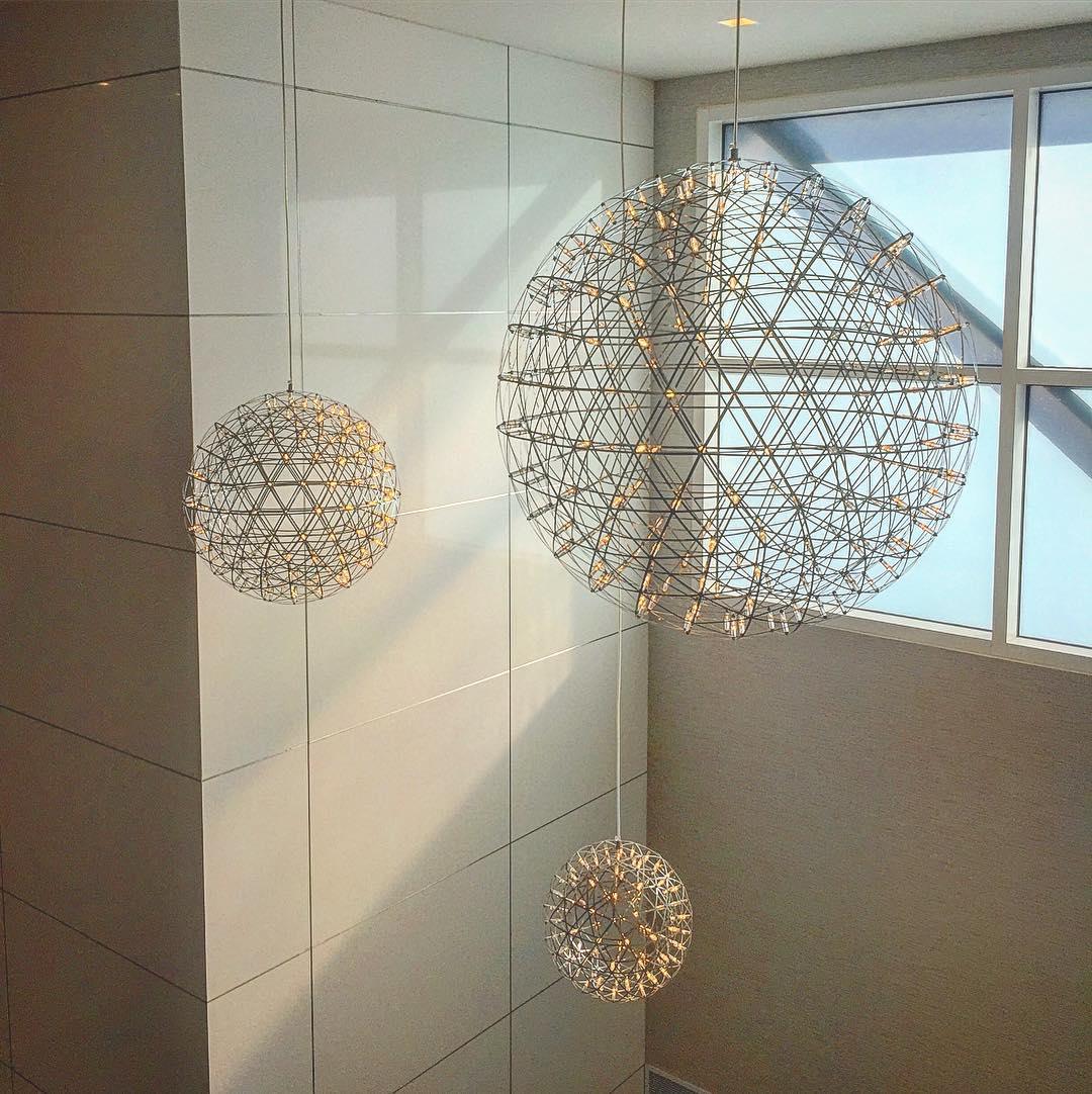 Three hanging lattice spheres in a tall void beside large windows and a tiled wall
