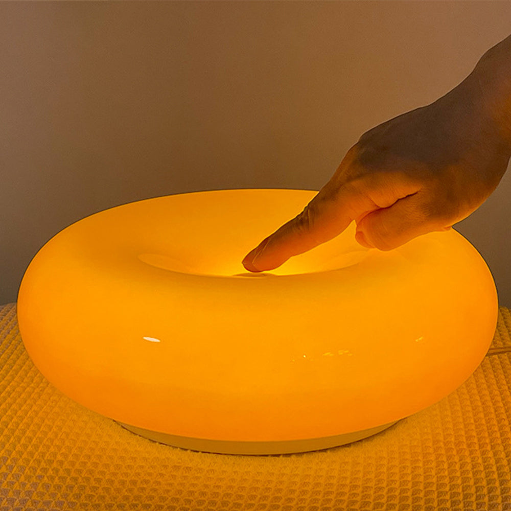 Hand reaching into the central well of the lit orange donut lamp on a woven cloth