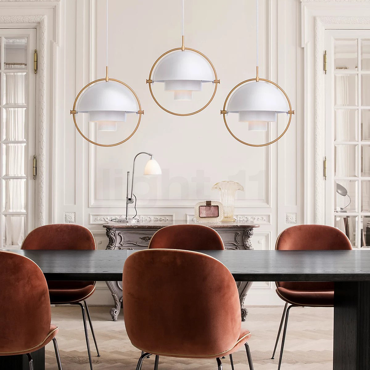Three white-and-gold ring pendants above a dark dining table and rust-coloured chairs.