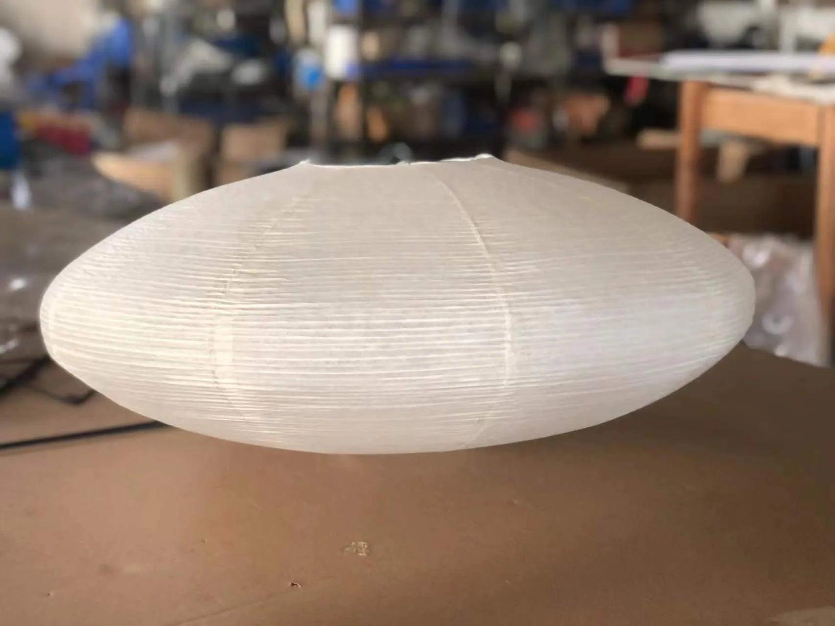 Detached-looking White paper shade resting on a brown worktable with workshop furniture behind