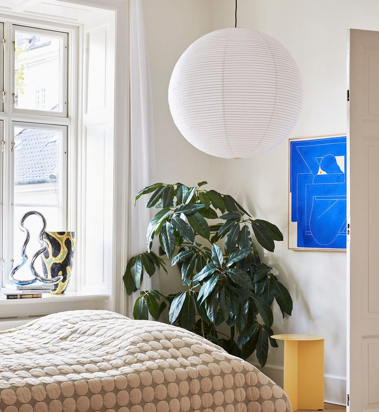White globe above a bed with patterned cover beside a large plant, blue artwork and chrome sculpture