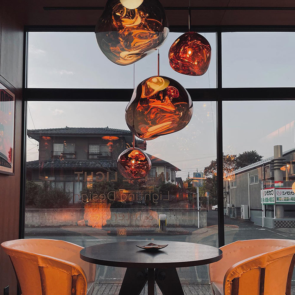 Mixed Rose Gold and Silver pendants above a dark round table and orange chairs beside a shop window
