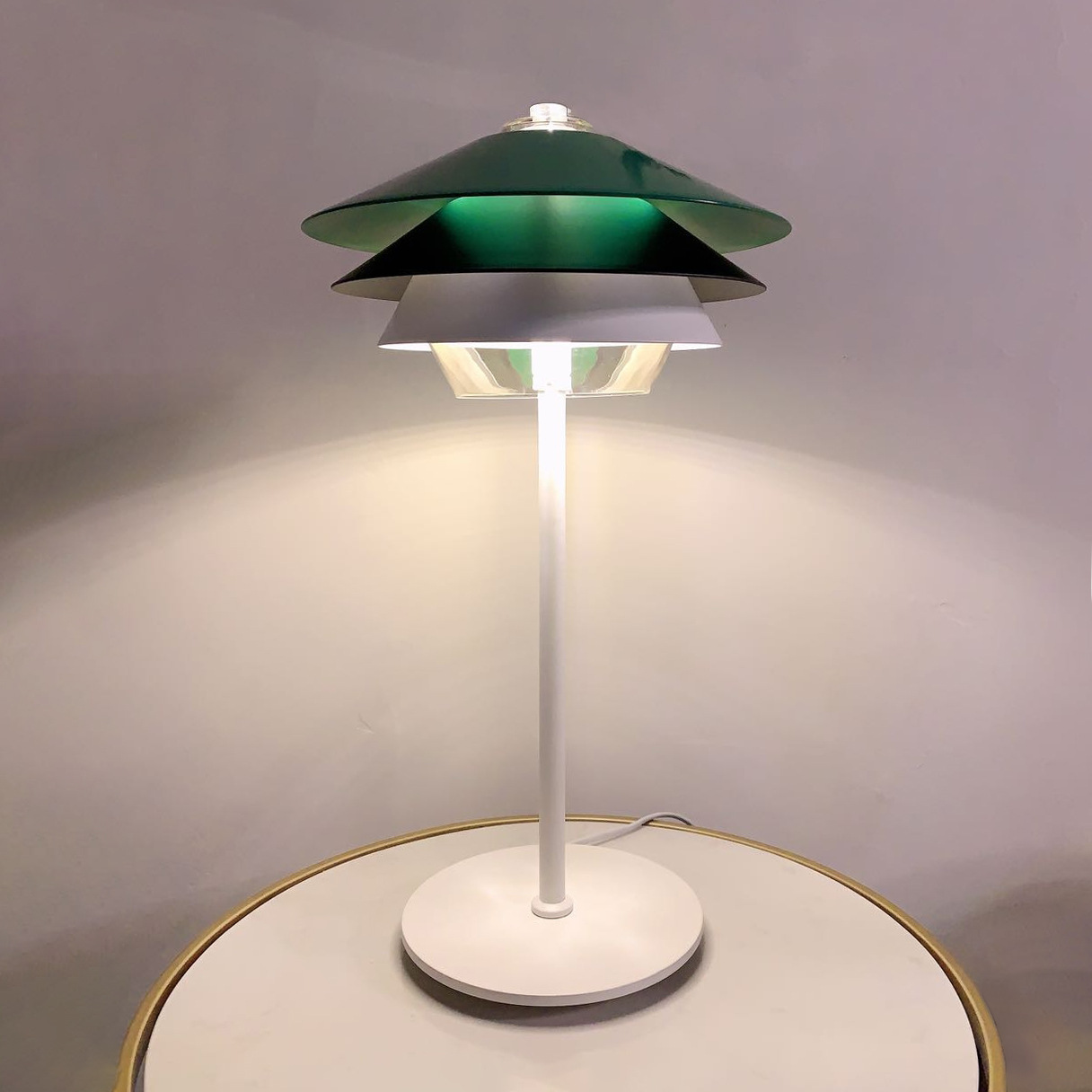 Lit Overlay lamp with green, black and white cones on a pale round table with a gold-coloured rim
